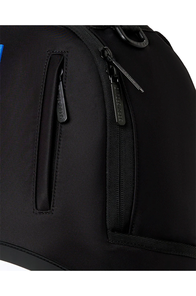 Close-up of a black nylon backpack showing two zippered pockets with black zipper pulls and a black metal D-ring on a white background.