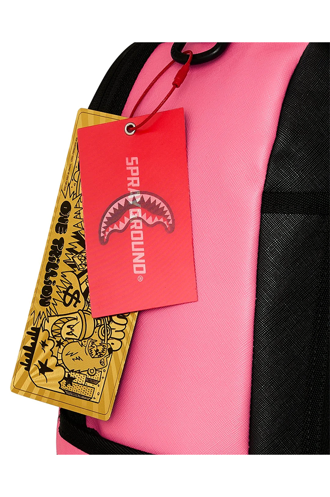 Close-up of a pink and black backpack with a red hangtag featuring the Shark Mouth logo and a yellow One Trillion tag with cartoon graphics.