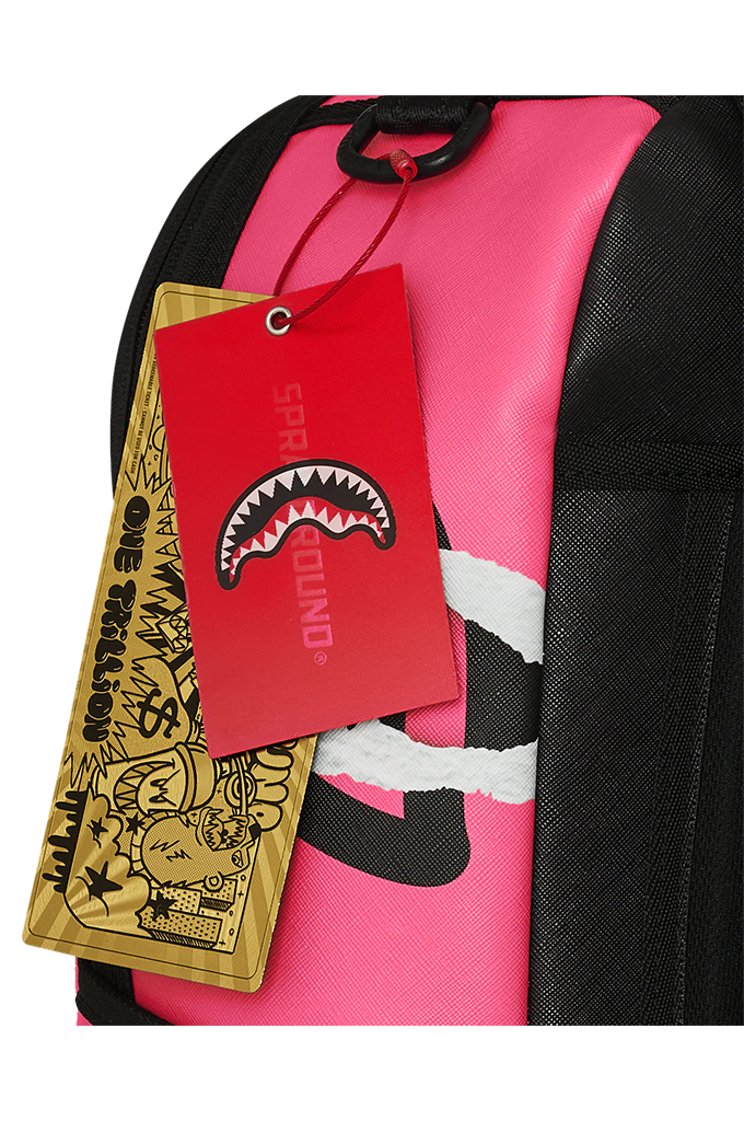 Close-up of a pink and black backpack with a red Sprayground tag featuring a shark mouth logo, and a gold hangtag with cartoon graphics.