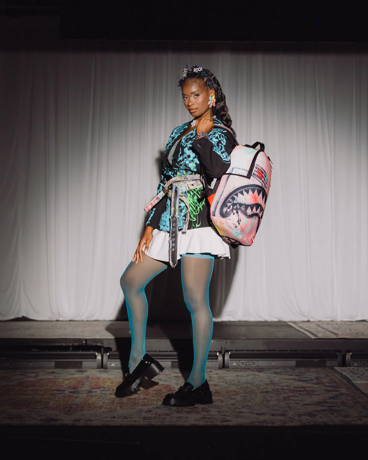 Model on a catwalk wearing a colorful outfit with a shark backpack.