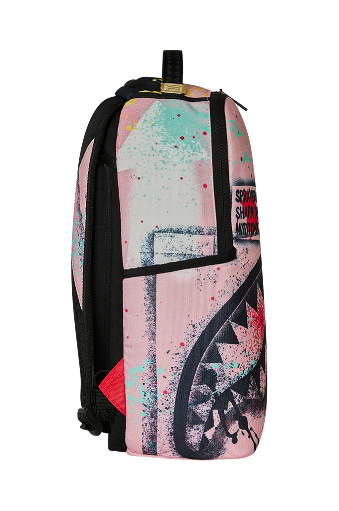 A backpack featuring a pink and black shark mouth graphic with paint splatters, shown against a plain white background.