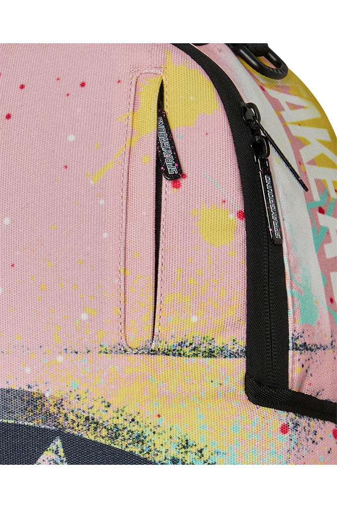 Close-up of a pink canvas backpack with a colorful paint splatter print, featuring a vertical zippered pocket and black zippers.
