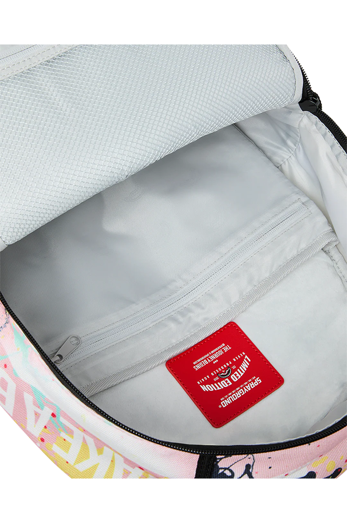 Close-up of the inside of a backpack showing a light gray interior lining, a zippered compartment, and a red sewn-in label. The exterior edge shows a pastel graphic print with pink, yellow, and blue tones.