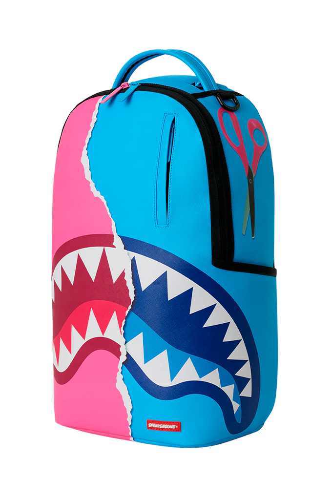 A Sprayground shark backpack in a vibrant pink and blue color-blocked design, featuring a large shark mouth graphic with white teeth across the lower half.