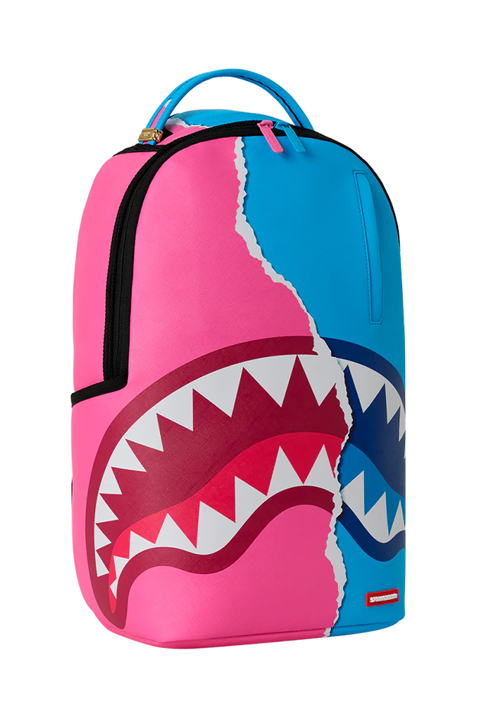 A Sprayground Shark backpack in a vibrant pink and blue color-blocked design, featuring a large shark mouth graphic with white teeth across the front.
