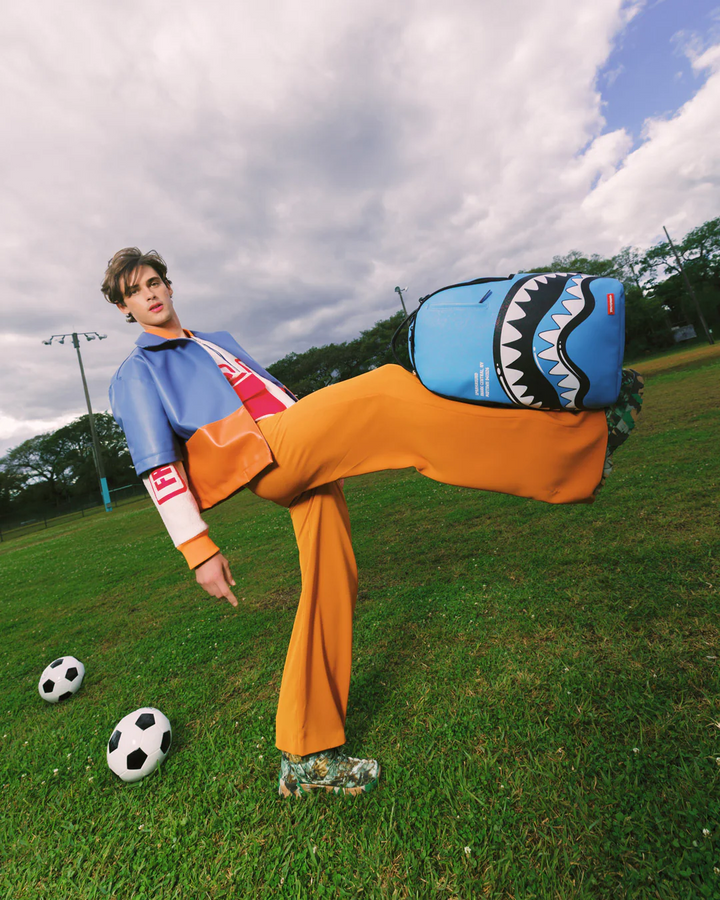 Person in colorful outfit with a shark-shaped bag on a grassy field