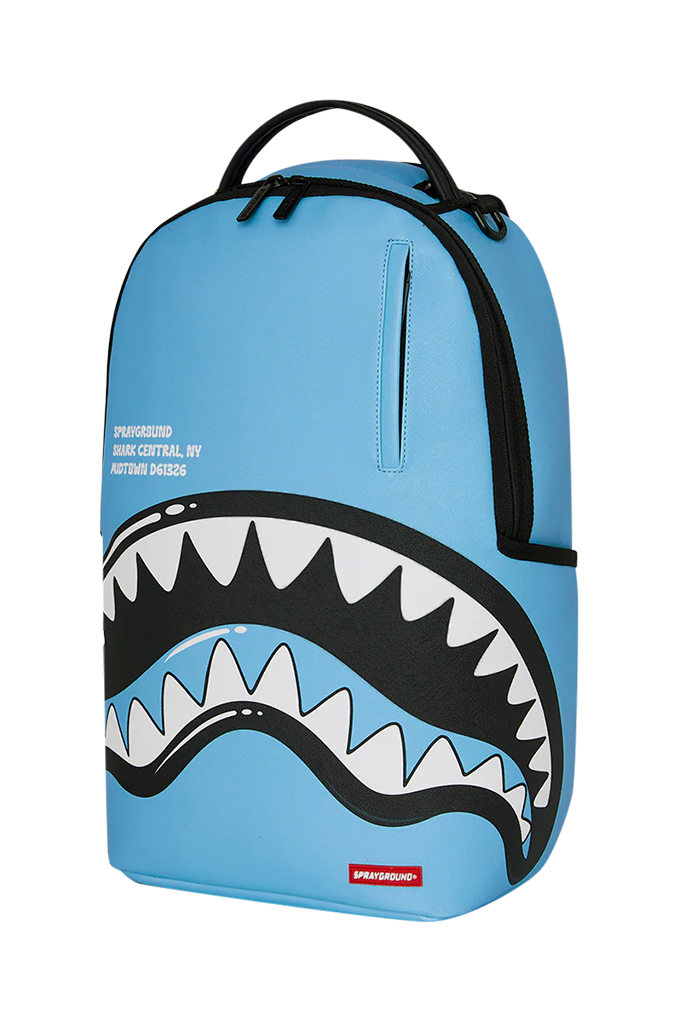 A light blue Sprayground backpack featuring a large shark mouth graphic with white teeth and black outlines on the front, complete with a top handle and a vertical zippered pocket.