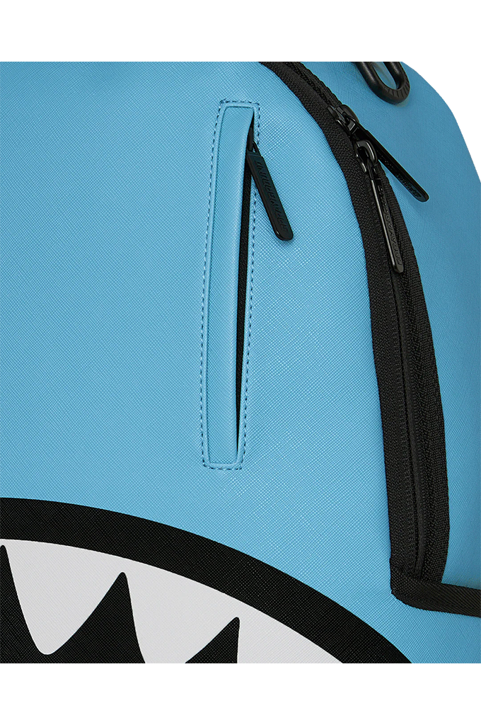Close-up of a light blue backpack featuring a vertical zippered pocket with a matching blue pull tab and black zippers, with part of a shark-face graphic visible at the bottom.