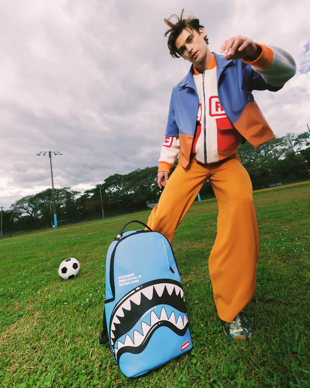 Person in colorful outfit with a shark-themed backpack on a grassy field