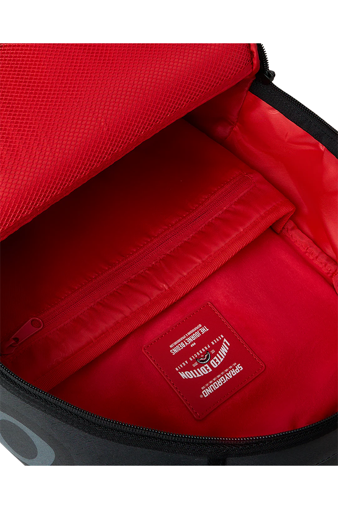 Close-up of the interior of a red backpack or bag, showing a zippered compartment, textured fabric lining, and a sewn-in label that reads Sprayground. 