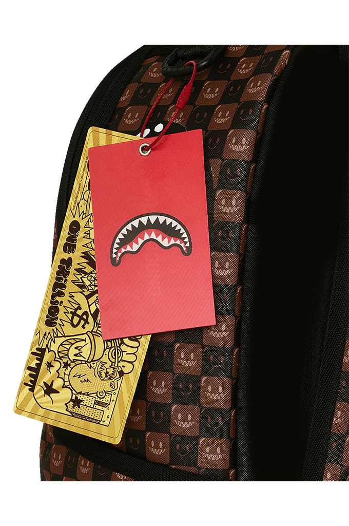 Close-up of a backpack with a brown and black checkered pattern featuring a shark face motif, a red hangtag with a shark mouth graphic, and a yellow paper tag with cartoon artwork.