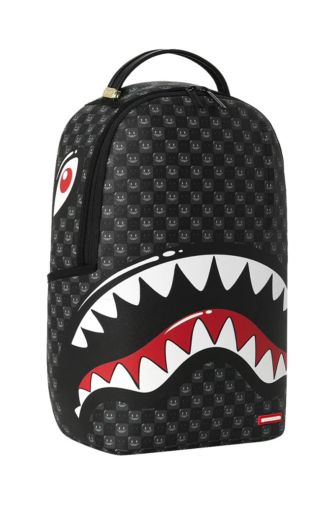 A black backpack featuring a repeating shark-face pattern and a large shark-mouth graphic on the front with white teeth, red interior, and a red accent stripe. A small red and white logo tag is visible near the bottom right corner.