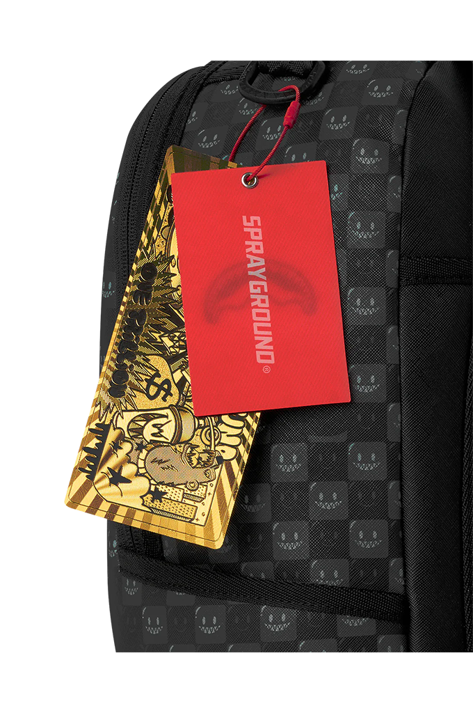 Close-up of a black backpack with a repeating smiley face pattern, featuring a red Sprayground hangtag and a gold patterned paper tag attached to the zipper area.