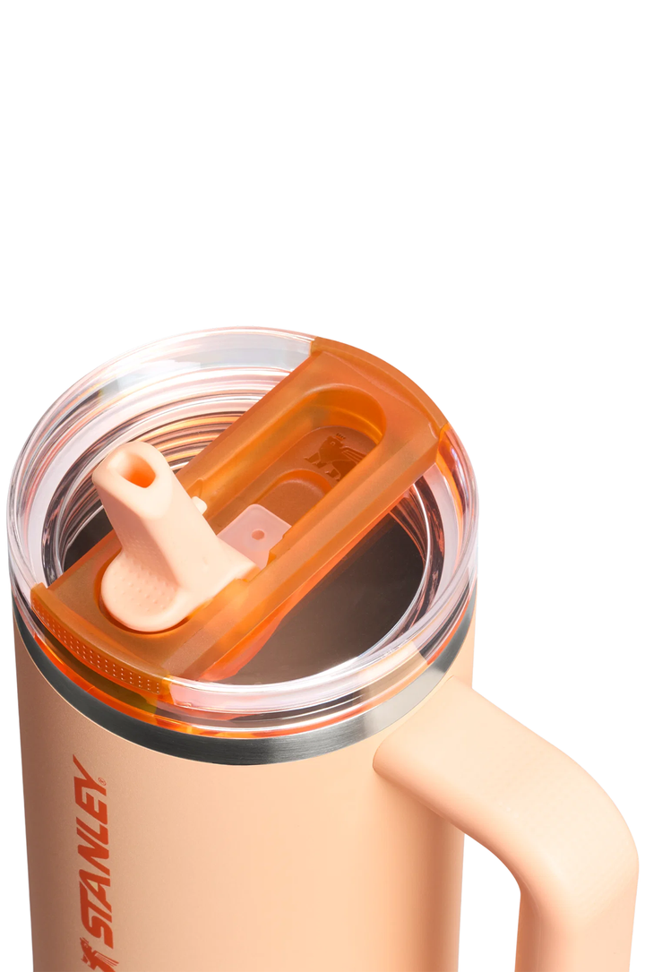Close-up of a Stanley insulated tumbler with a peach-colored body, clear lid, and orange translucent flip straw cover on a white background.#color_orange-sherbet