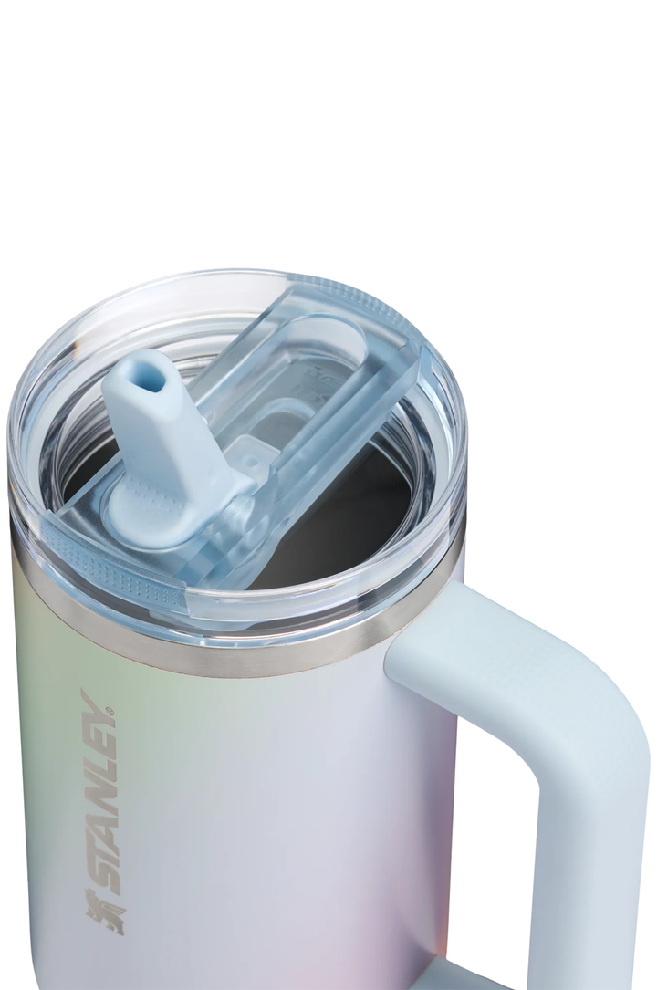 Close-up of a Stanley insulated tumbler with a clear lid and light blue flip straw, featuring a pale iridescent body and a side handle on a white background.#color_sunrise-spiral