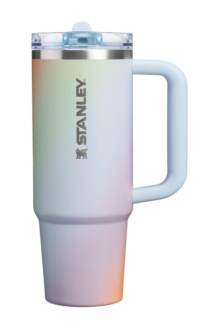 Stanley travel tumbler with a pastel rainbow gradient finish, featuring a light blue handle and lid, and the Stanley logo printed vertically on the front.#color_sunrise-spiral