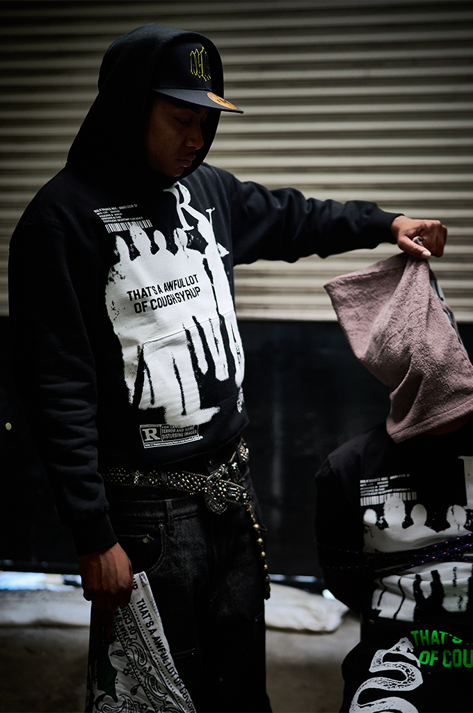 Man wearing a black That's A Awful Lot Of Cough Syrup streetwear hoodie and a black baseball cap.