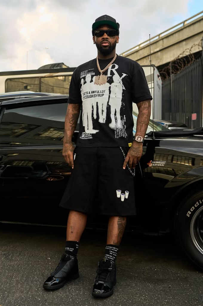 Model wearing a black That's An Awful Lot Of Cough Syrup t-shirt paired with matching black streetwear shorts and black high-top sneakers.