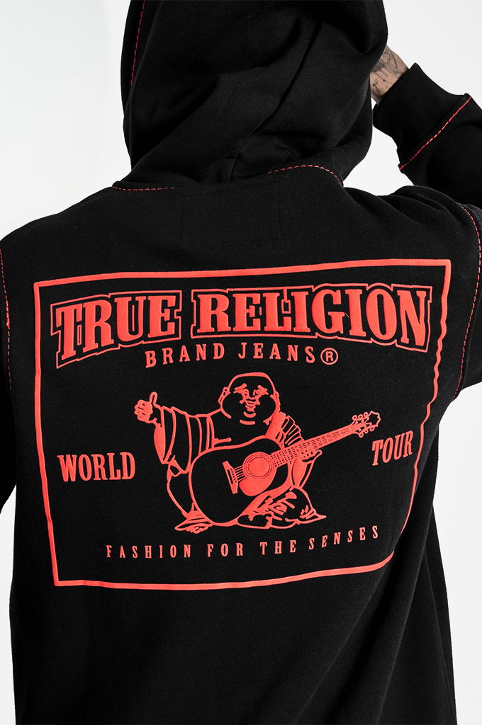 Close-up back view of a black hoodie with a large red True Religion graphic on the back, featuring the brand name, a seated figure playing guitar, and 'World Tour' text.