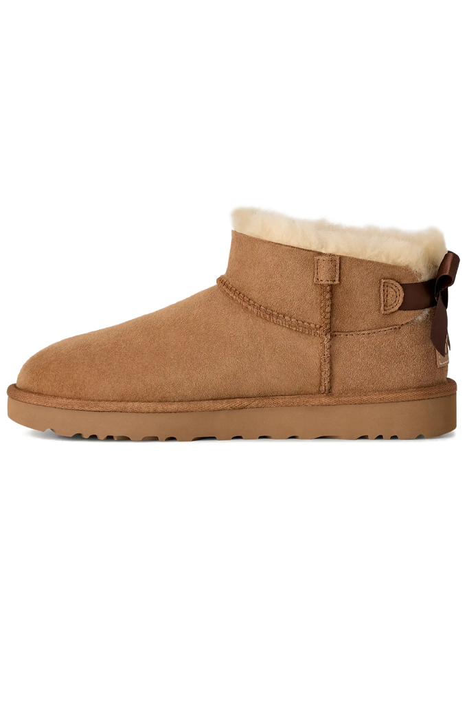 A classic brown suede ankle boot with a soft cream shearling lining and a brown leather side bow, shown in profile against a white background.