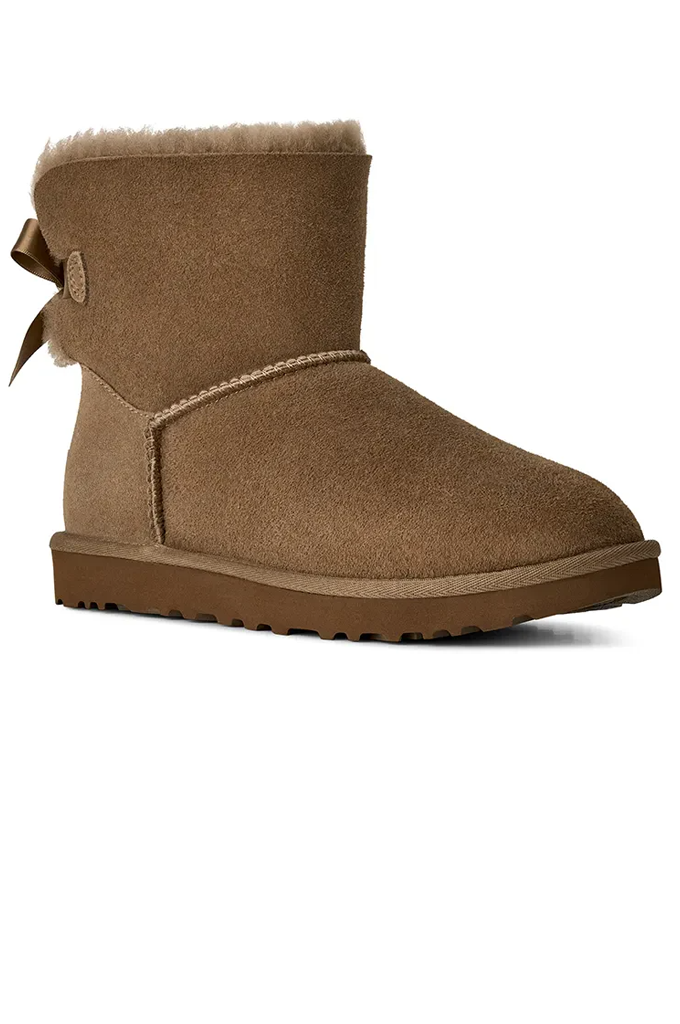 A single brown suede ankle boot with a matching brown faux-leather bow on the back, a light tan shearling lining, and a brown sole, shown against a plain white background.#color_light-bronze