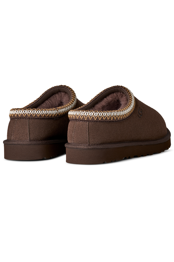 A pair of brown slip-on slippers with a textured knit trim around the collar, shown from a three-quarters angle on a white background.#color_dusted-cocoa
