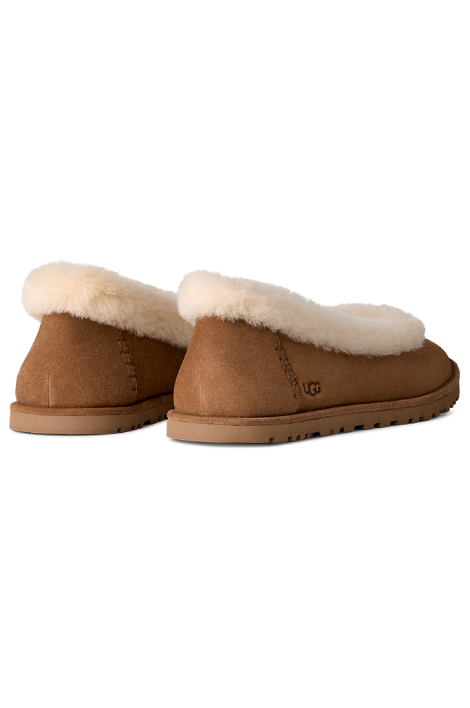 A pair of UGG slip-on slippers in tan suede with a soft white shearling lining, shown from a rear three-quarter angle on a plain white background.