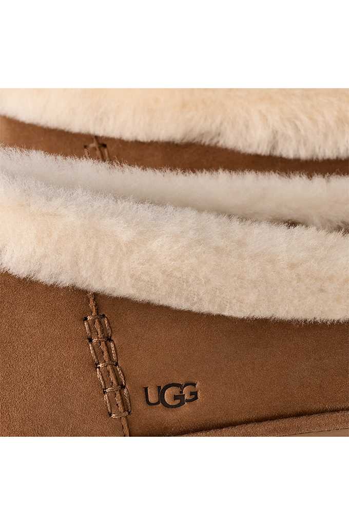 Close-up of a UGG boot showing the tan suede exterior, white shearling lining, and the black UGG logo on the side.