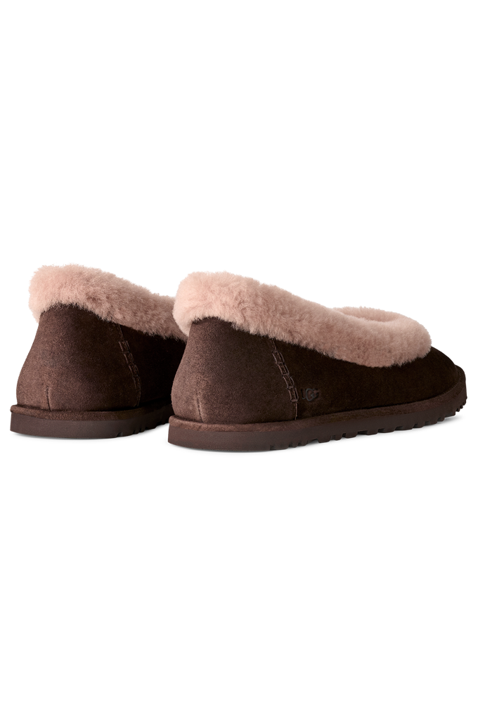 A pair of dark brown slip-on slippers with a soft, light beige shearling-style lining visible at the opening, shown from a rear three-quarter angle on a white background.