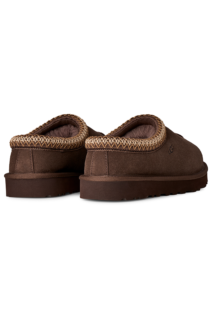 A pair of brown slip-on slippers with a textured knit trim around the collar, shown from a side-rear angle on a plain white background.#color_dusted-cocoa