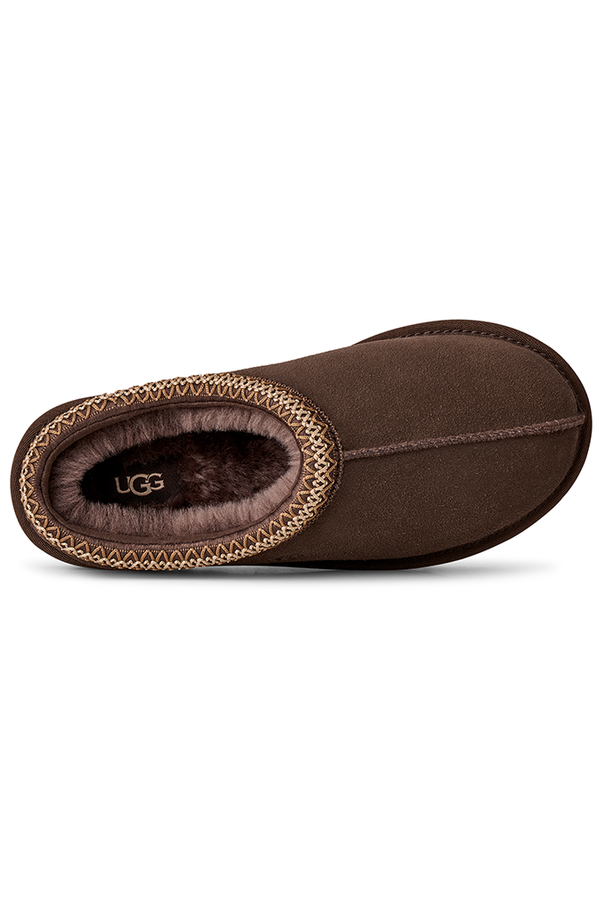 A single brown suede slipper shown from a side profile view on a white background, featuring a braided trim and a plush brown faux fur interior with the UGG logo visible.#color_dusted-cocoa