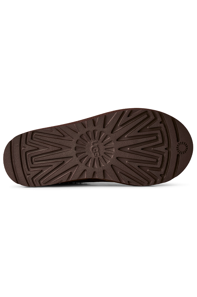A close-up, top-down view of a dark brown textured rubber shoe sole, showing the tread pattern and a small circular logo on the heel.#color_dusted-cocoa