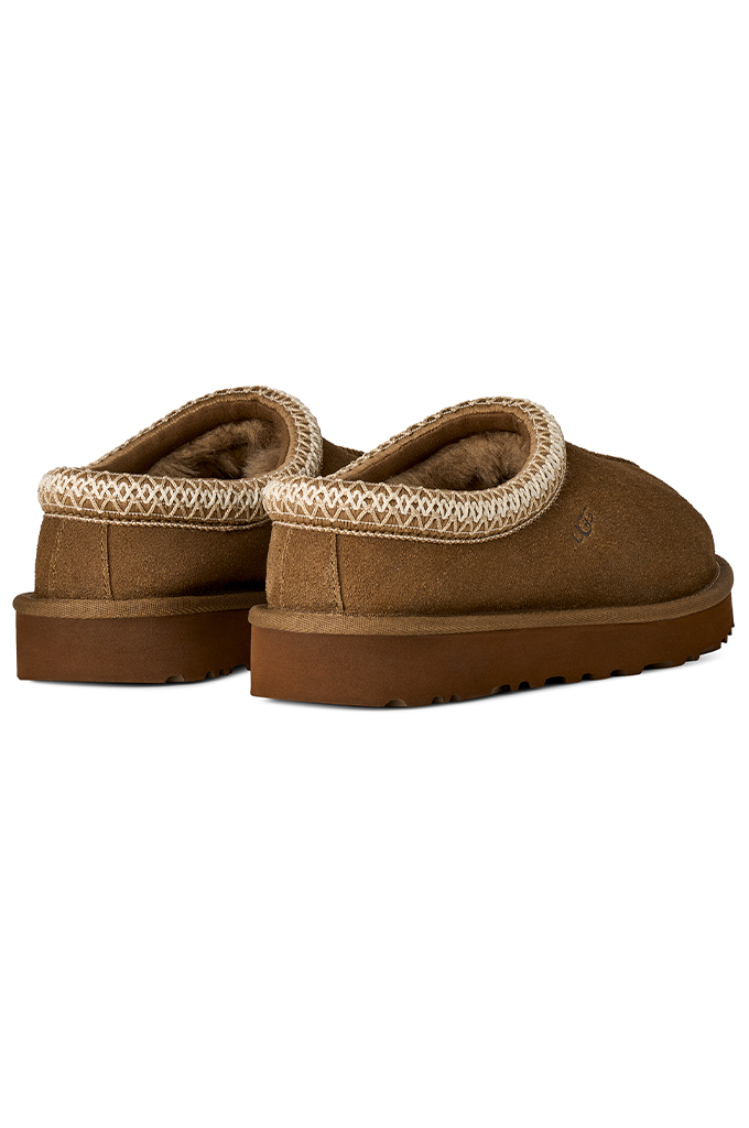 A pair of brown suede slip-on slippers with a beige patterned trim around the collar and a brown sole, shown against a plain white background.#color_light-bronze