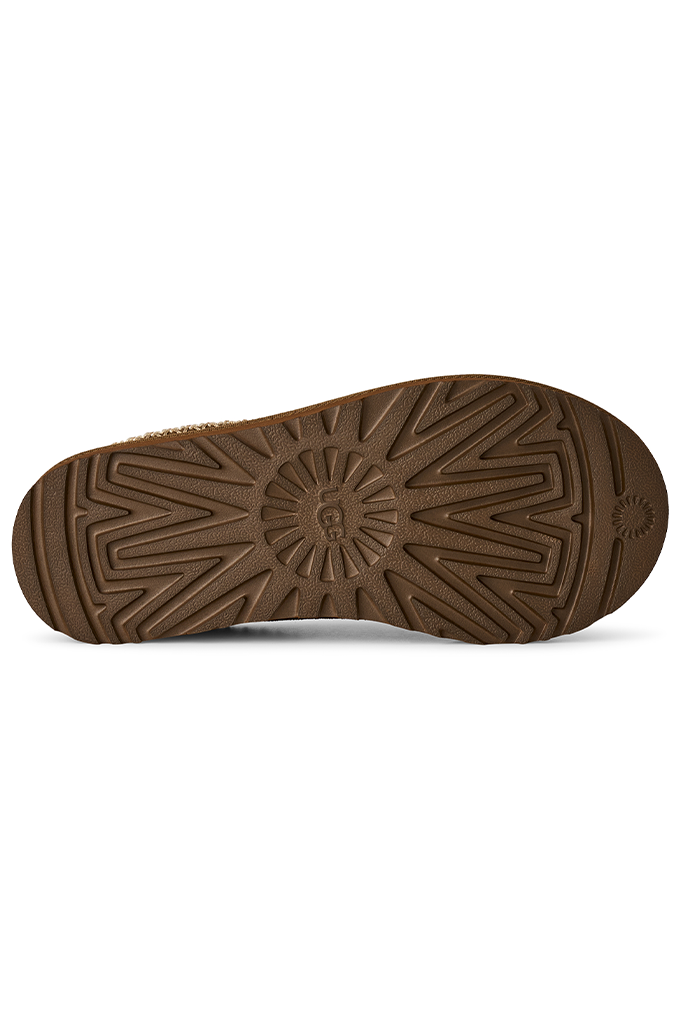 A close-up, top-down view of a brown rubber shoe sole with a textured tread pattern and a small embossed logo near the heel, set against a plain white background.#color_light-bronze