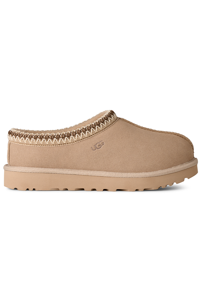 A single beige UGG slip-on clog shoe with a textured suede upper, decorative braided trim, and a thick lug sole, shown against a plain white background.#color_moonlight