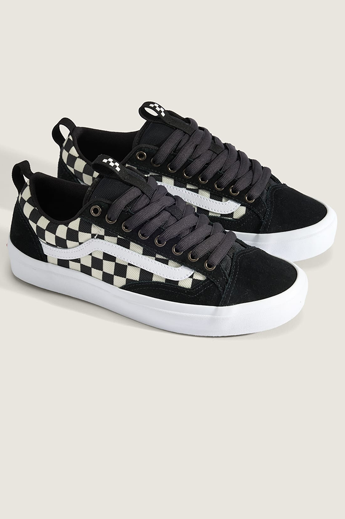A pair of Vans platform sneakers in black suede with a black and white checkerboard side stripe, black laces, and thick white platform soles, set against a light beige background.