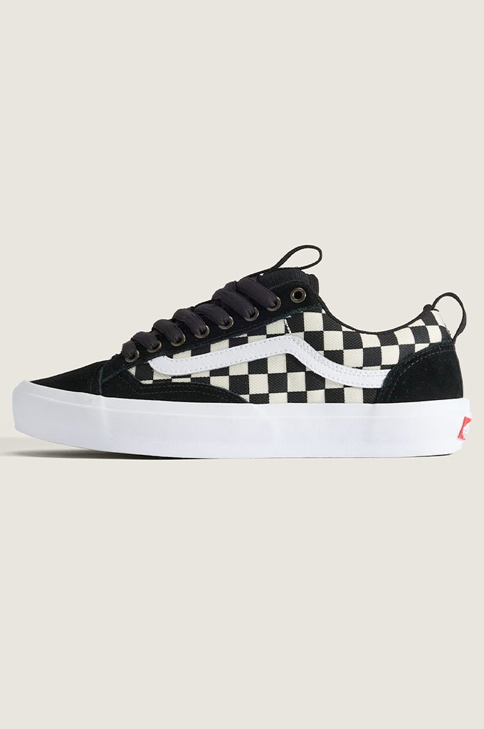 A single Vans Old Skool sneaker in black and white checkerboard canvas with black suede overlays, black laces, and a thick white rubber sole, shown against a light beige background.