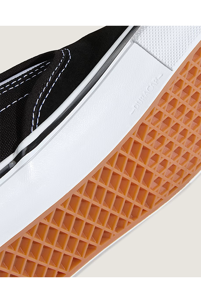 Close-up of a Vans platform sneaker showing the black canvas upper, white midsole, and orange gum rubber sole.