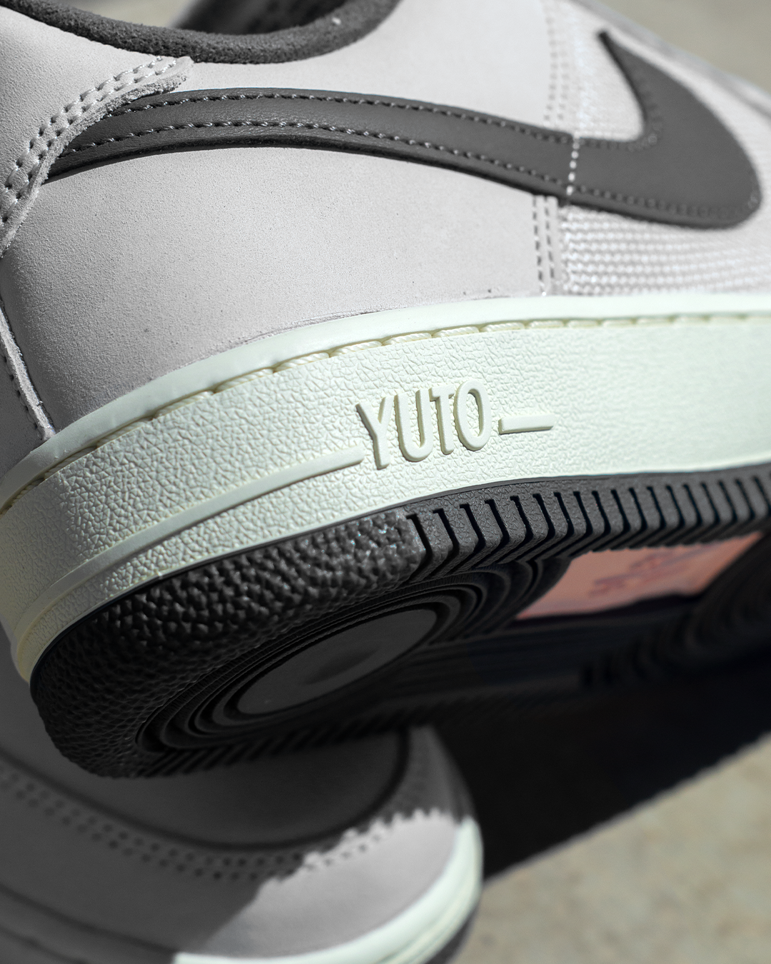 Close-up of a Nike YUTO sneaker showing the side profile with a light gray leather upper, dark gray Swoosh, and a thick off-white midsole embossed with 'YUTO'.